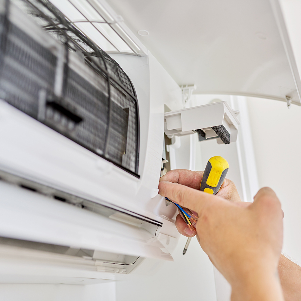 An electrician's hand holding a screwdriver and wiring up the internal unit of an Air2Air heat pump system.