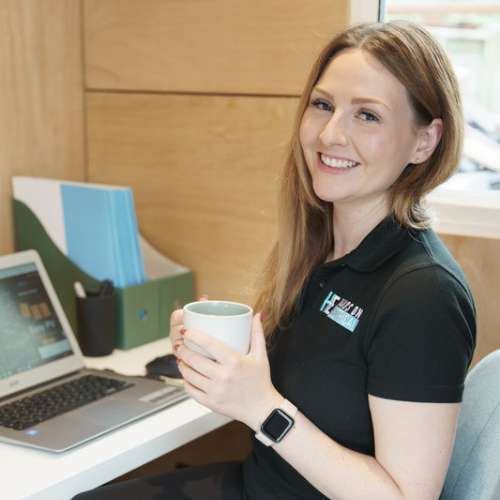 Cheryl Hands, office manager at Hands On Electrical, smiling at her desk with a coffee mug.