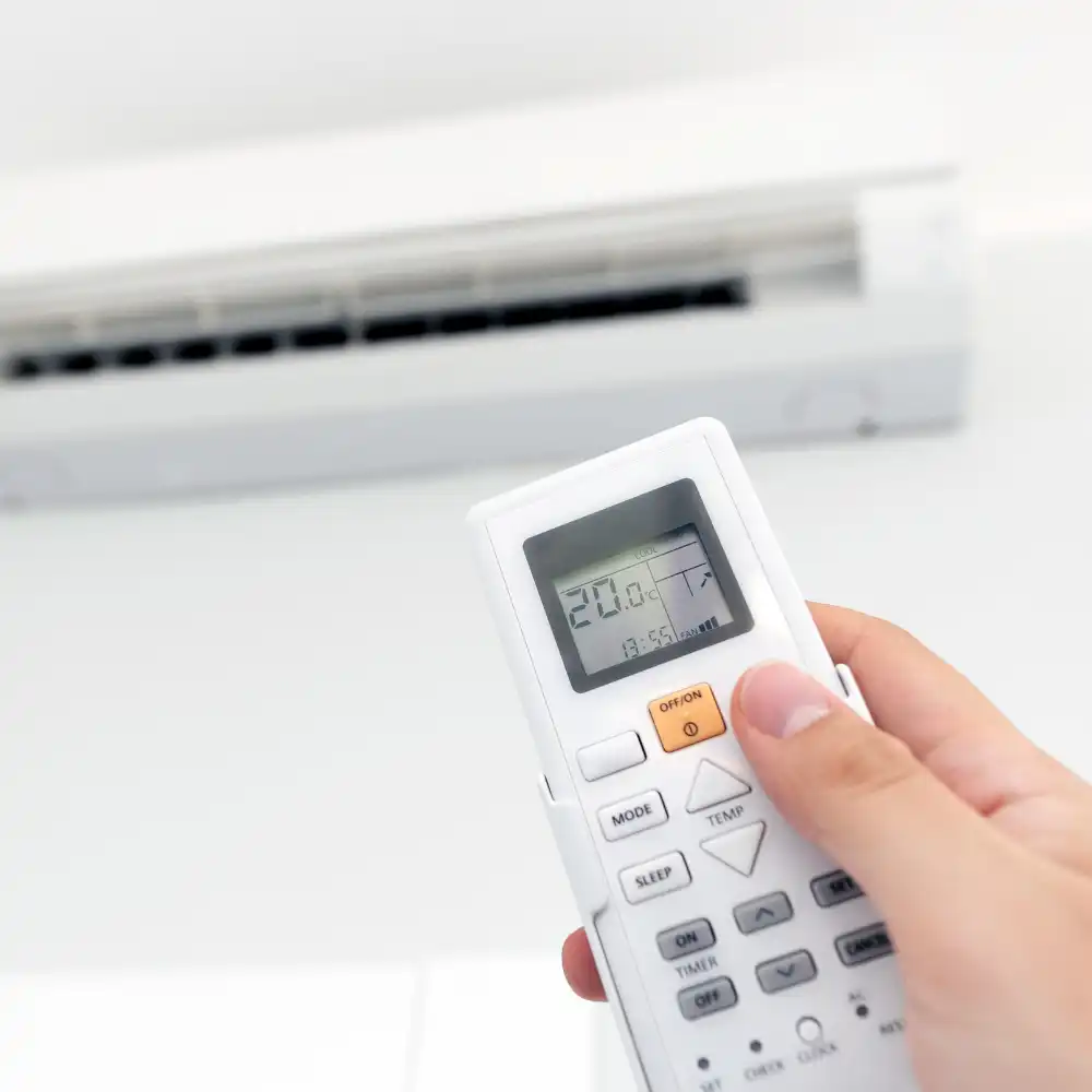 A hand adjusting the temperature settings on an Air2Air heat pump using a remote control, installed by Hands On Electrical.